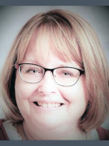 Zoomed in headshot of Champion of the Month Tracy Dock-Masanz smiling in front of a gray wall.