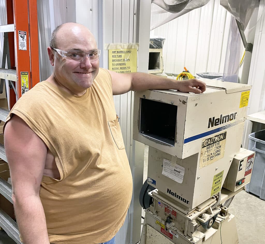 Joey Affolter Westfall smiles while he rests one arm on machinery at his workplace, Federal Premium Ammunition.