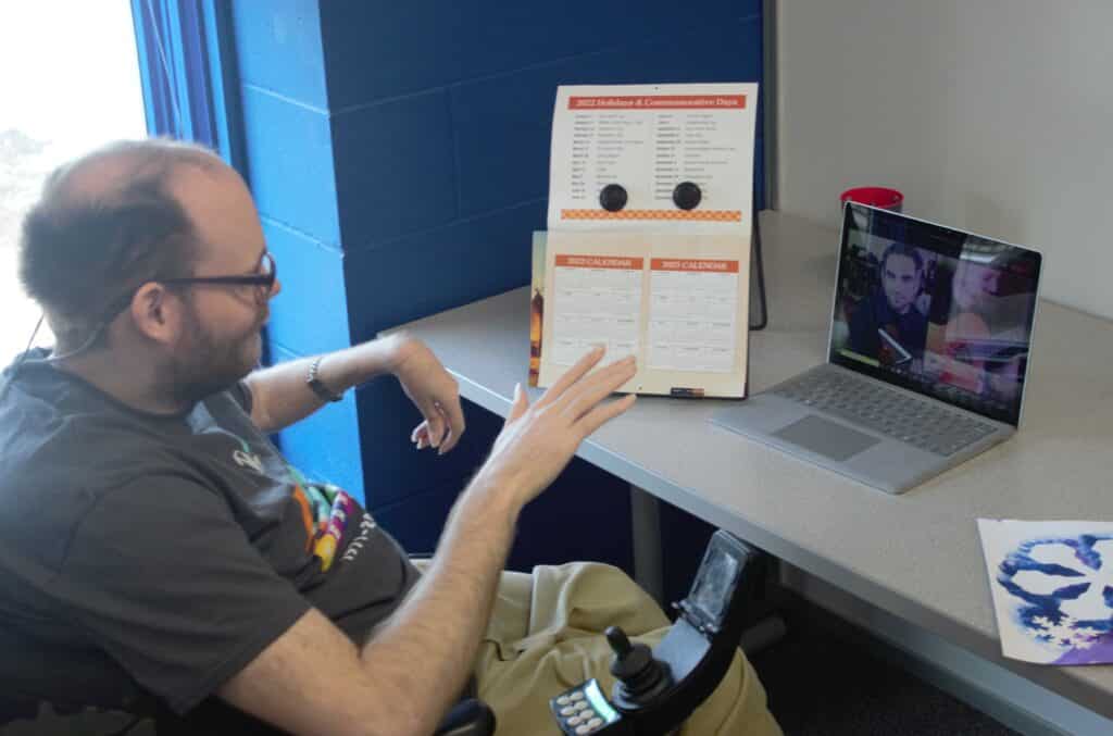 Man in wheelchair enjoys connection with friends on his computer screen.