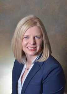 Dr. Marcy Young Illies, a white woman with blonde hair wearing a navy blue suit jacket, poses for a professional headshot.