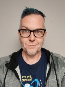 Daniel Klonowski, a man with light skin, short dark hair, and gray facial hair, wears dark-rimmed glasses and a gray sweatshirt,
