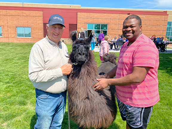 Two men stand next to a black and brown llama smiling.