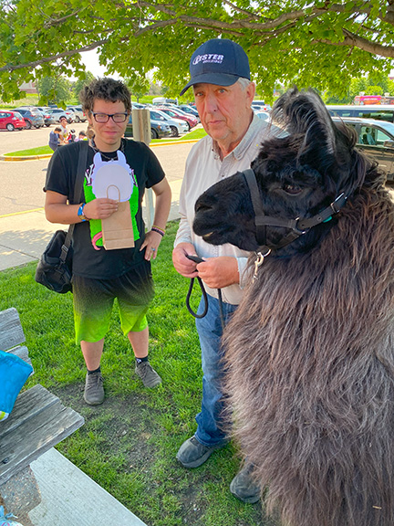 Two men stand next to a black and brown colored llama.