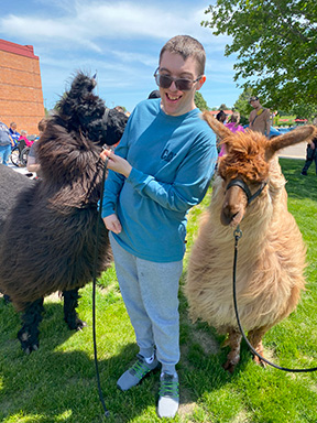 A person served by Rise stands outside smiling next to two llamas.