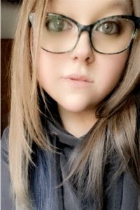 close selfie of woman with long brown hair and black-rimmed glasses