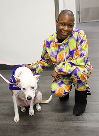 Person served by Rise kneeling down on the ground and smiling as they pet a visiting therapy dog.