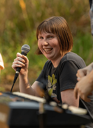 Person served by Rise in a park smiling and holding a microphone.