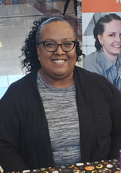 Kimberly Washington smiles wearing black glasses, a gray top, and a black sweater.