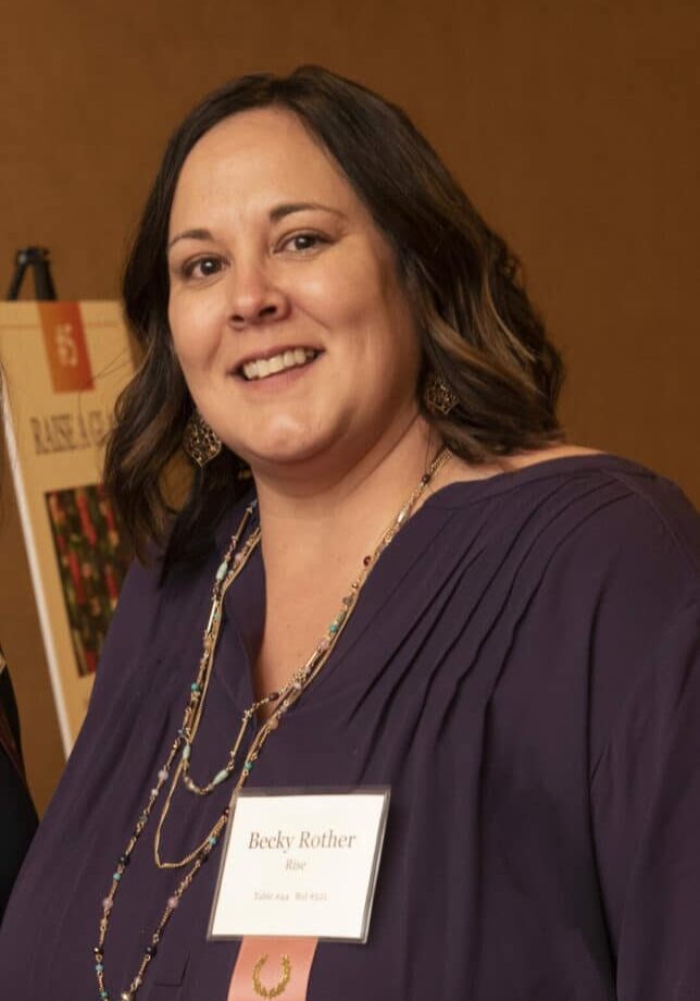 Becky Rother smiles at a Rise gala wearing a name tag and a black blouse.