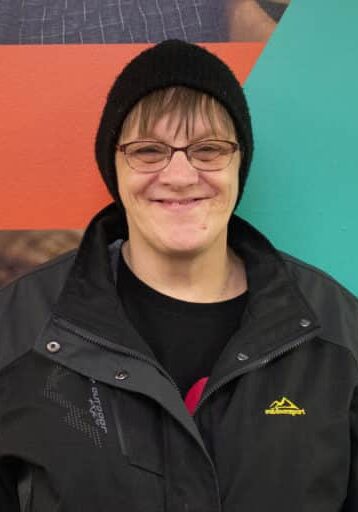 Shari Happel smiles in front of a Rise branded wall wearing a black beanie hat and black jacket.