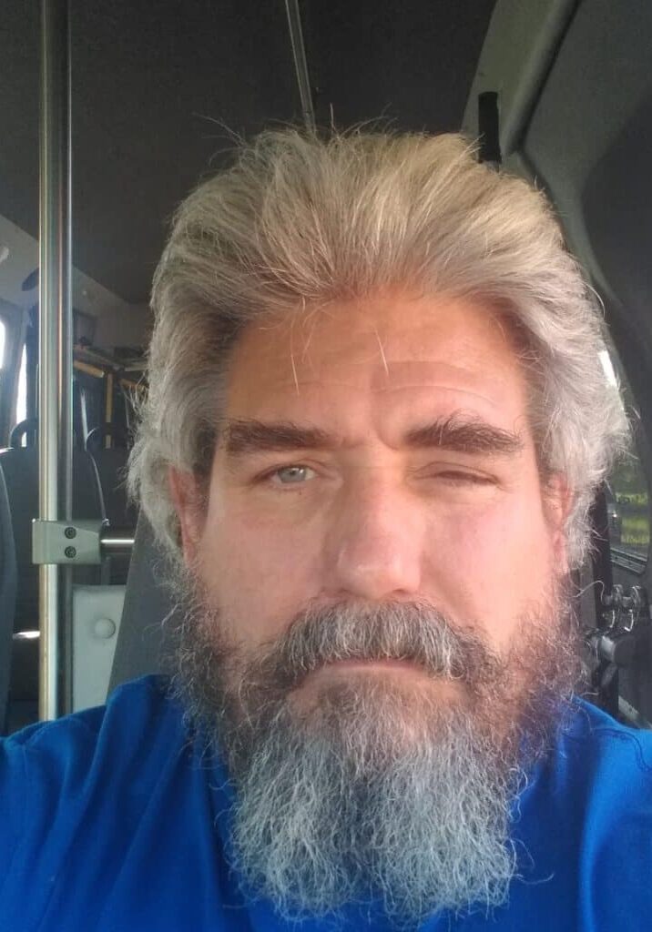 Portrait photo of Ronald Woolcott wearing a blue shirt and sitting in the drivers seat of a Rise bus.