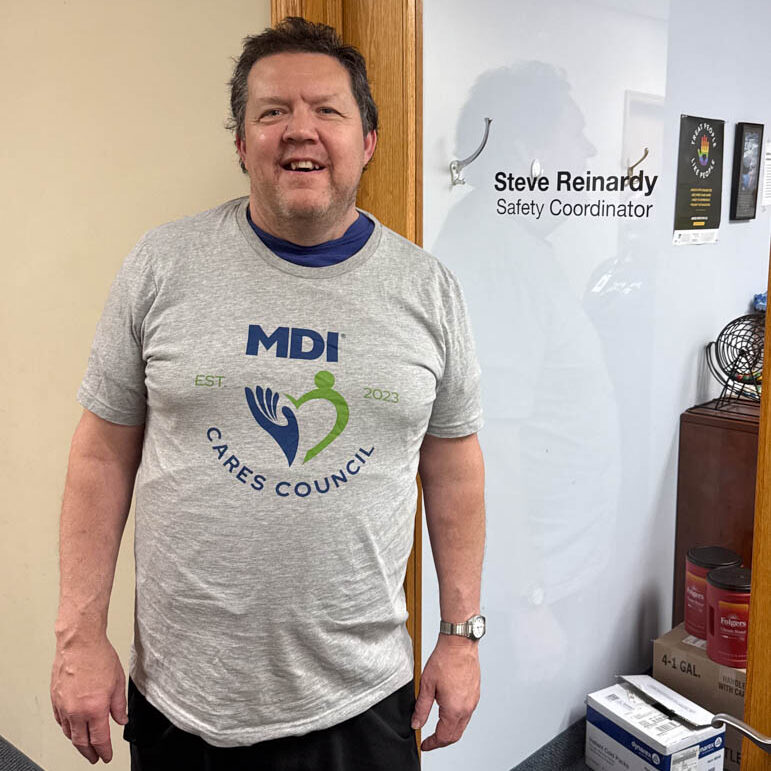 Steve wearing a grey MDI t-shirt standing in front of the door to his office.