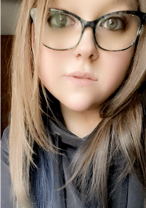 close selfie of woman with long brown hair and black-rimmed glasses