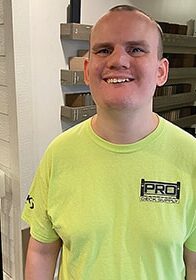 Alex White smiles in a fluorescent green shirt as he stands in the deck and basement showroom.