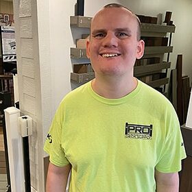 Alex White smiles in a fluorescent green shirt as he stands in the deck and basement showroom.