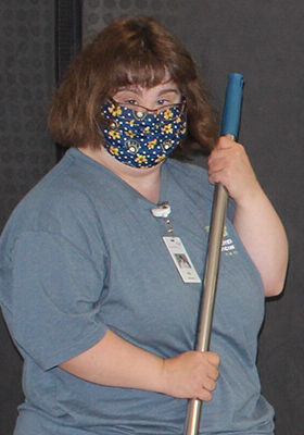 Allie Rumpel wears a blue and yellow printed mask while holding a mop.