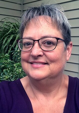 Amber Barnes smiles outside of her home wearing glasses and a navy blue top.