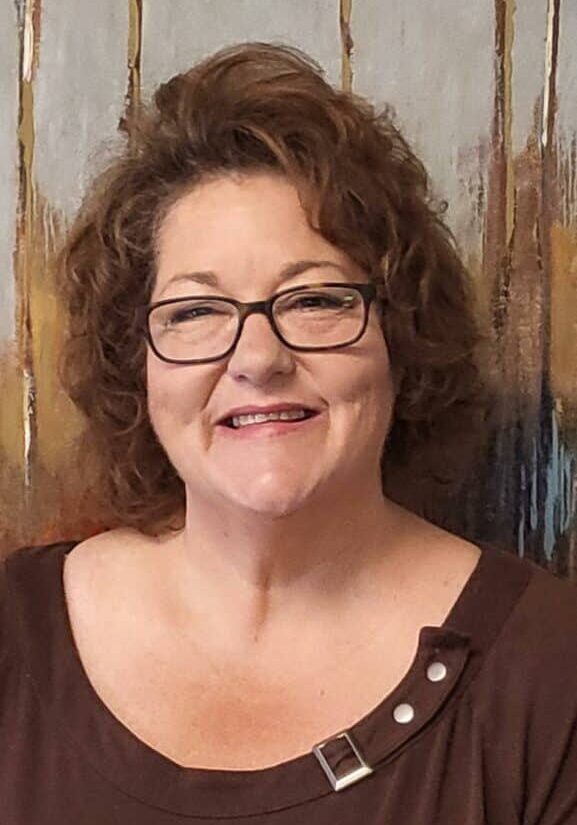 Amy Johnson, a white woman with short brown hair wearing glasses and a brown shirt, smiling for the camera