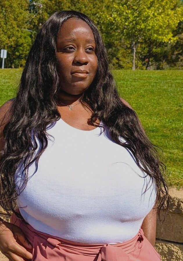 Andrea Ash smiles in front of a grass background wearing a white tank top and pink pants.