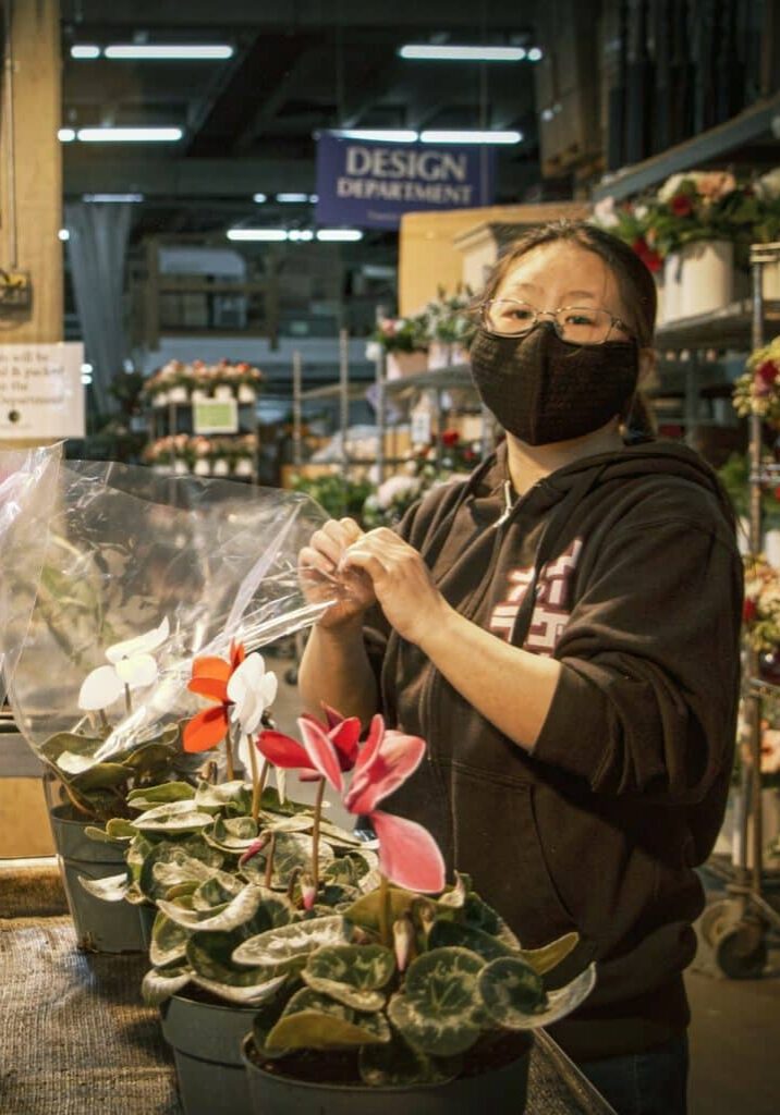 Angela Yang wears a mask while arranging flowerpots inside her workplace warehouse.