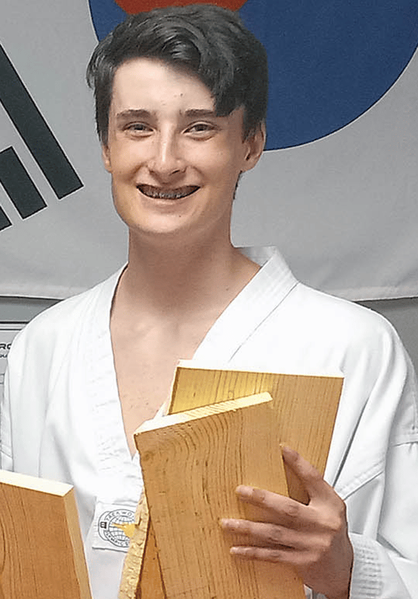 Dominic Buckingham smiles wearing a taekwondo outfit holding small boards of wood.