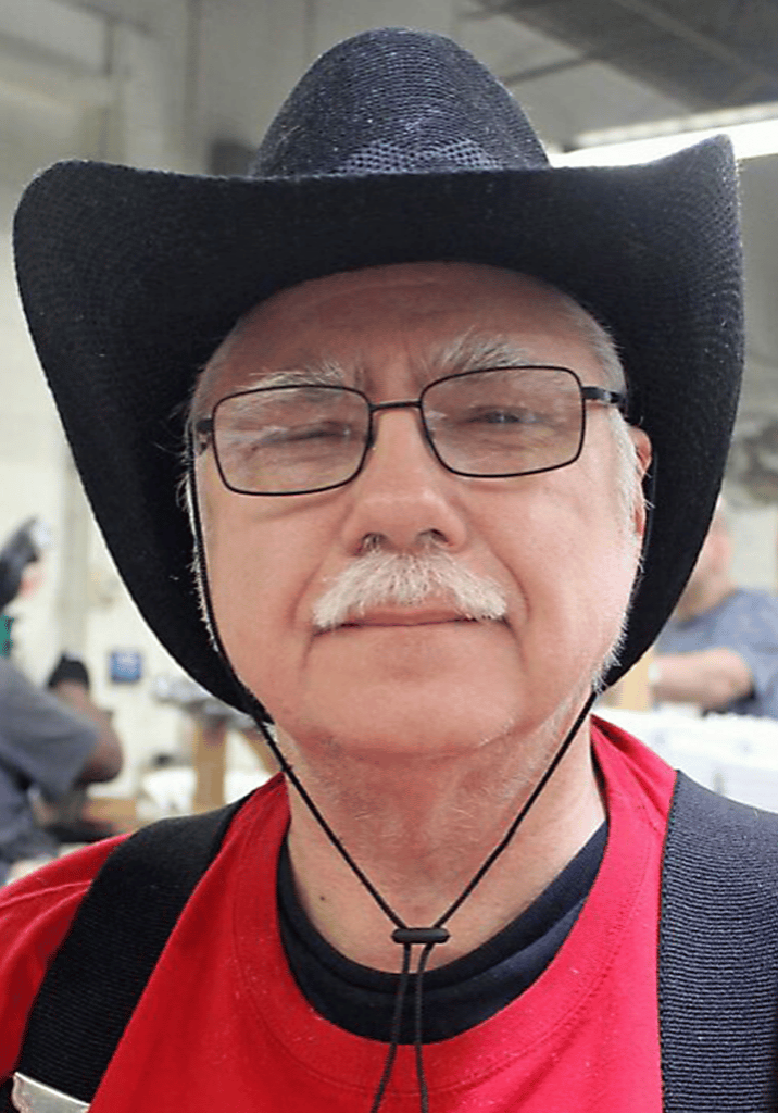 Eddie Ridge smiles wearing a black cowboy hat and glasses in his workplace.