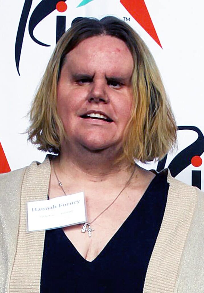 Hannah Furney Smiles wearing a black dress and a gold sweater in front of a Rise branded backdrop.