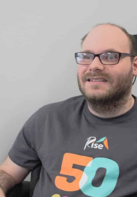 Man wearing glasses sits in wheelchair and smiles for the camera.