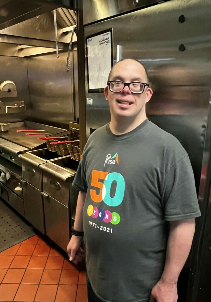 Jason smiles in front of the kitchen where he works at Stacy Sports Grill.