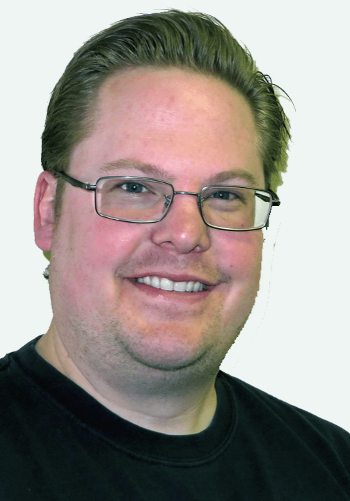 Jebb Anderson headshot smiling in front of a white wall wearing glasses and a black t-shirt.