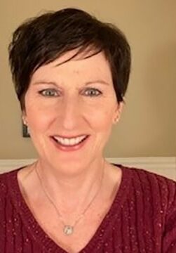 Kathleen Voss smiles wearing a maroon sweater in front of a tan and white wall.