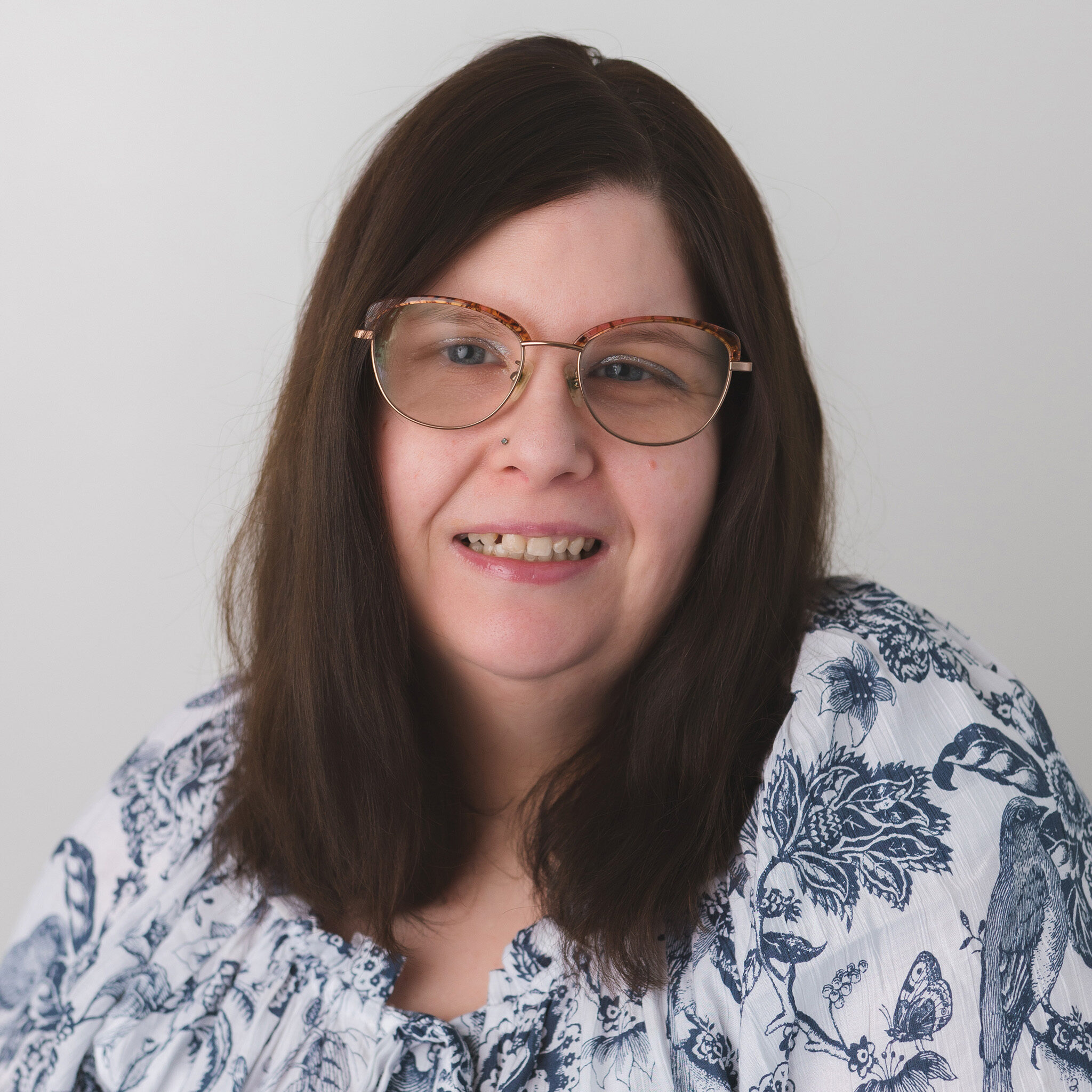 Katie McDermott smiling at the camera while wearing glasses and a blue and white top.