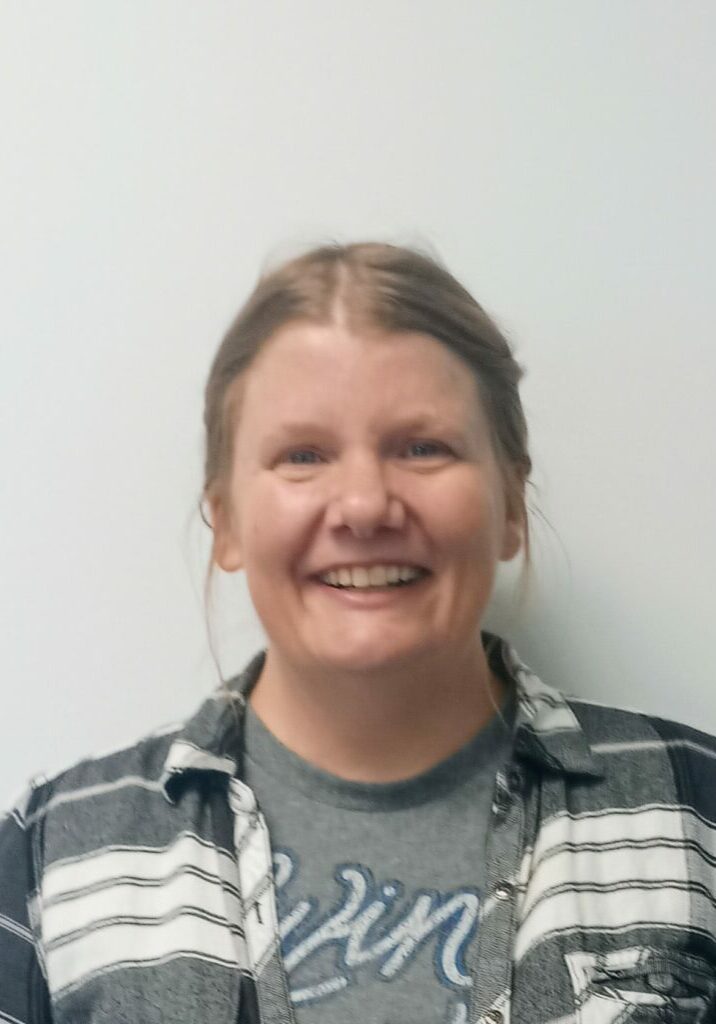 Kelli Johnson, a white woman with blonde hair, wears a gray and white striped shirt and smiles for the camera.