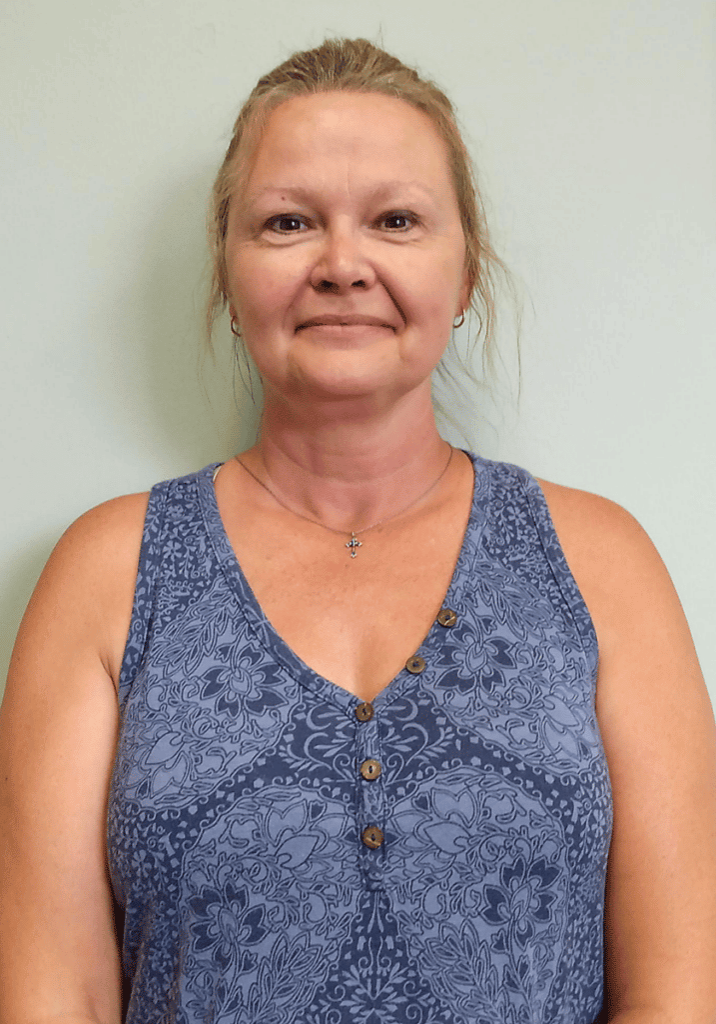 Kim Ersland smiles in front of a white wall wearing a blue floral top.