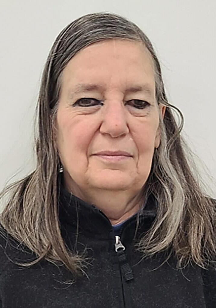 Kim Hultgren smiles in front of a light gray background wearing a black zip up sweater.