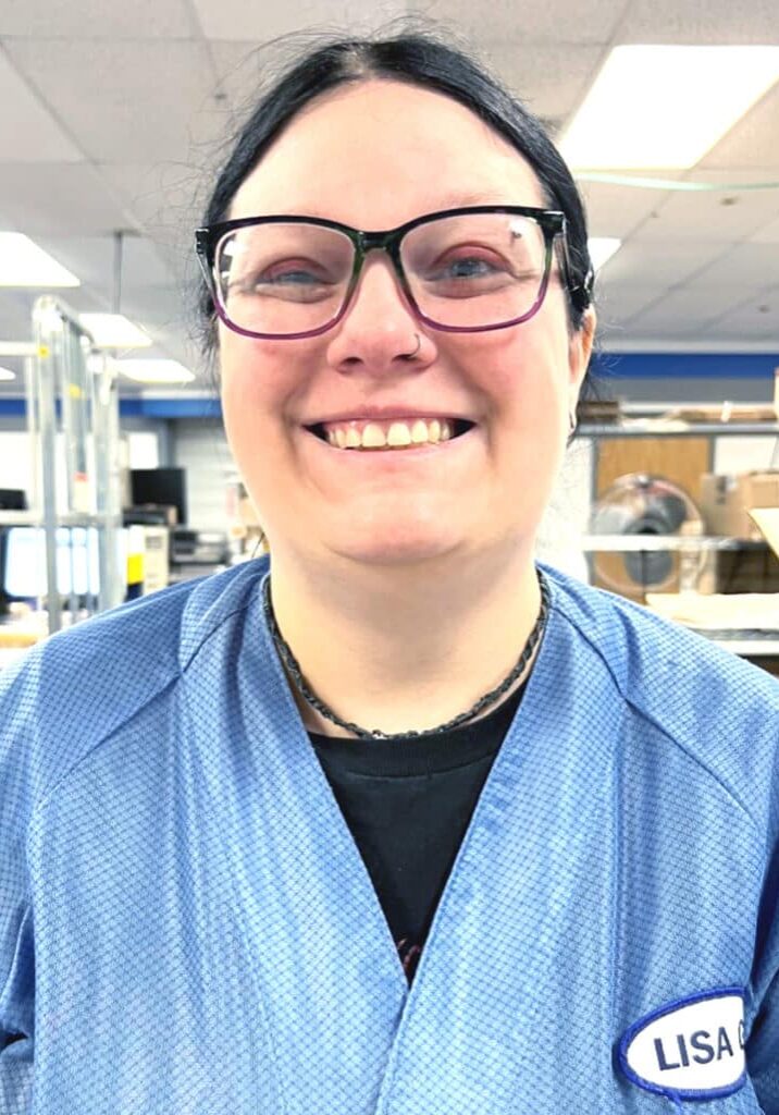 Lisa Geng smiles wearing a blue shirt with her name on it and large purple and black glasses.