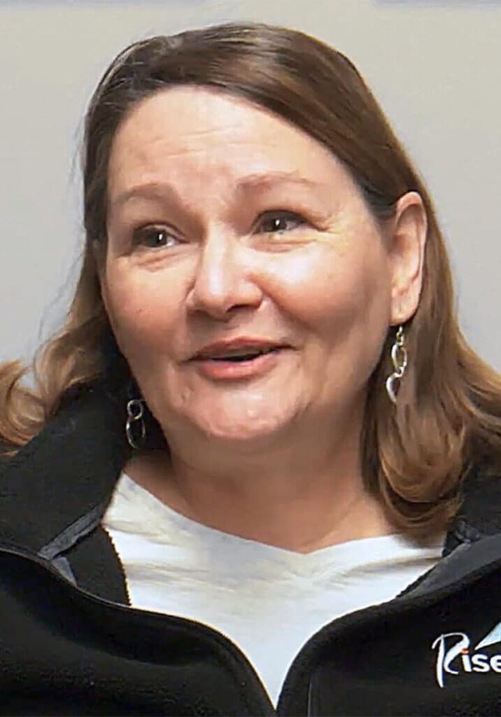 Lori Clauson wears a Rise sweatshirt as she smiles in front of a gray background.