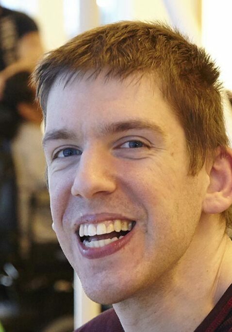 White man with red-brown hair smiles for the camera