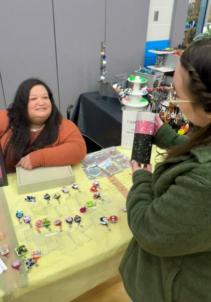 Rachel Dolan speaks with a customer at a craft fair for her business, Rachel's Bling N' Thingz