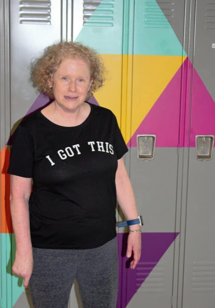 Rosanne smiles in front of lockers with Rise colored triangles: pink, yellow, blue, orange, and purple.