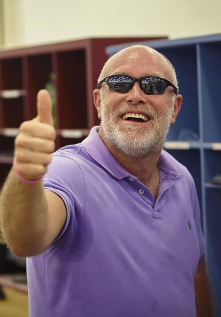 Sean Lovejoy holds a thumbs up pose as he smiles wearing purple shirt and sunglasses.