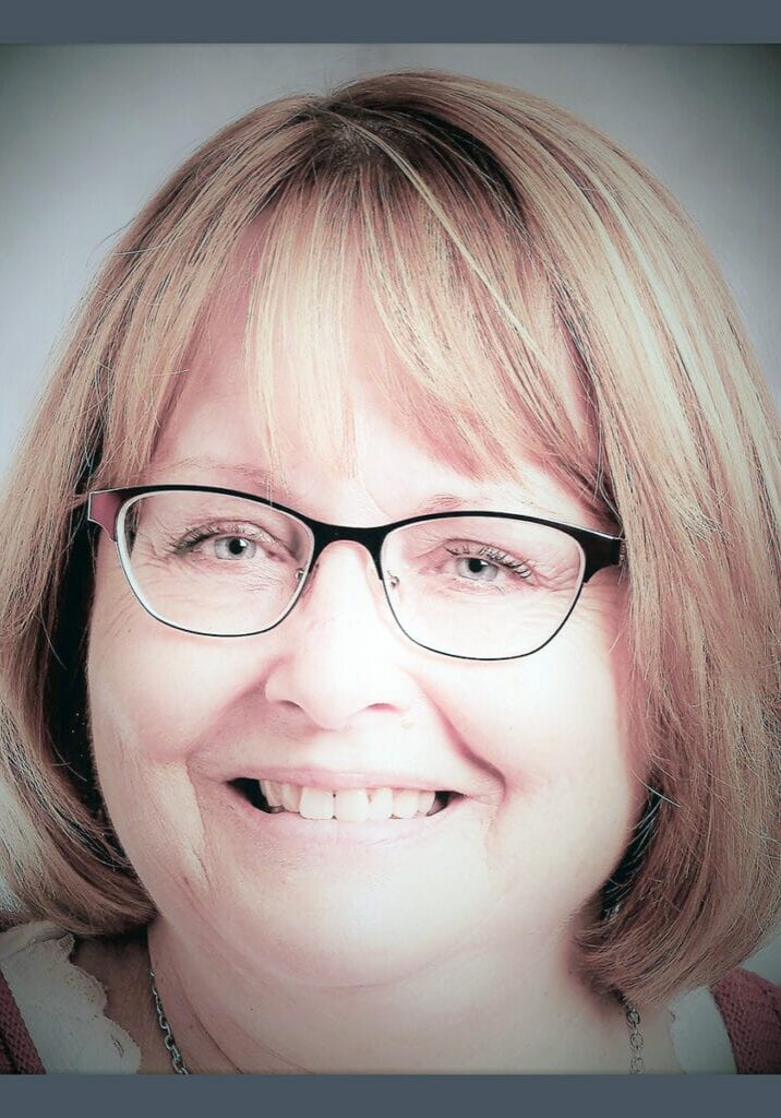 Zoomed in headshot of Champion of the Month Tracy Dock-Masanz smiling in front of a gray wall.