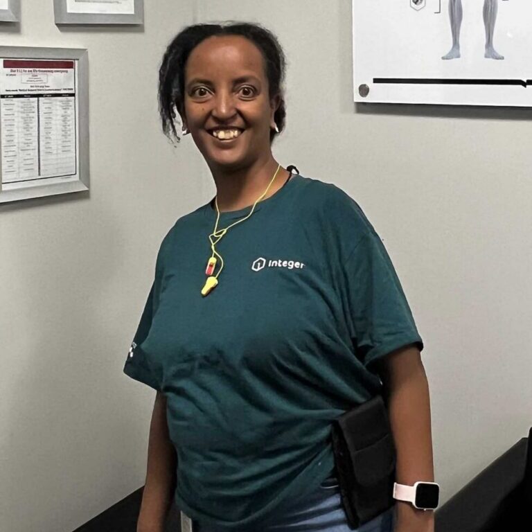 Tsega smiles in front of a gray wall wearing a dark teal shirt.