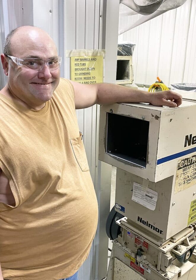 Joey Affolter Westfall smiles while he rests one arm on machinery at his workplace, Federal Premium Ammunition.