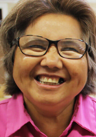 Tan woman with brown hair and glasses wearing a pink shirt smiles for the camera.