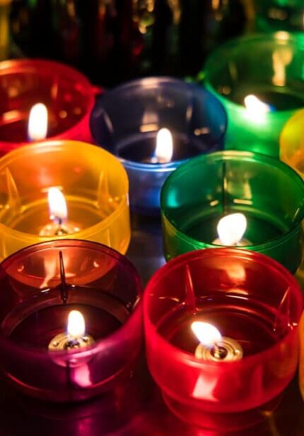 An array of colorful candles have their wicks burning in a dark room.