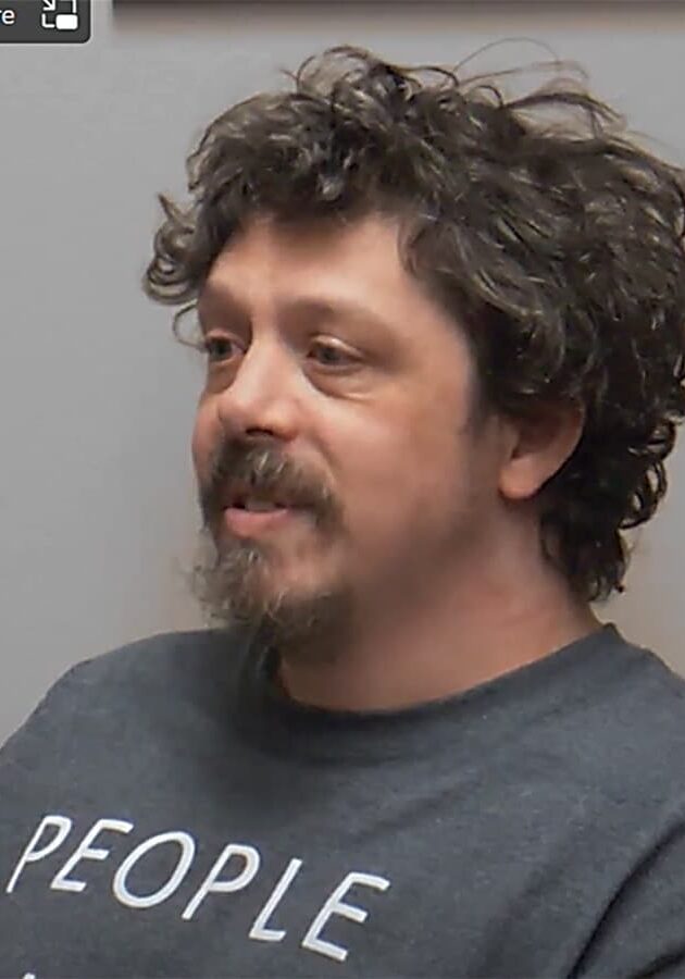 Ryan Sawyer sits in front of a gray background wearing a dark gray shirt.